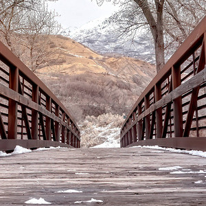 方形作物在冬季观看的金属栏杆桥木着陆上融化的雪在背景中可以看到白雪皑的山丘和树木与阴云密背景图片