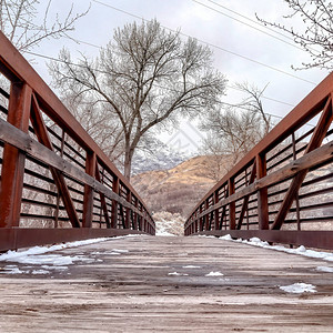 在冬天观看的金属栏杆桥木着陆的方形融雪在背景中可以看到白雪皑的山丘和树木与阴云密背景图片