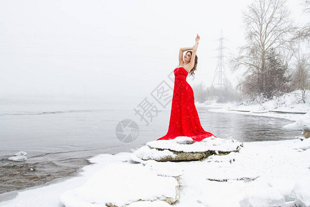 年轻穿长红色裙子的女孩站在雪河图片