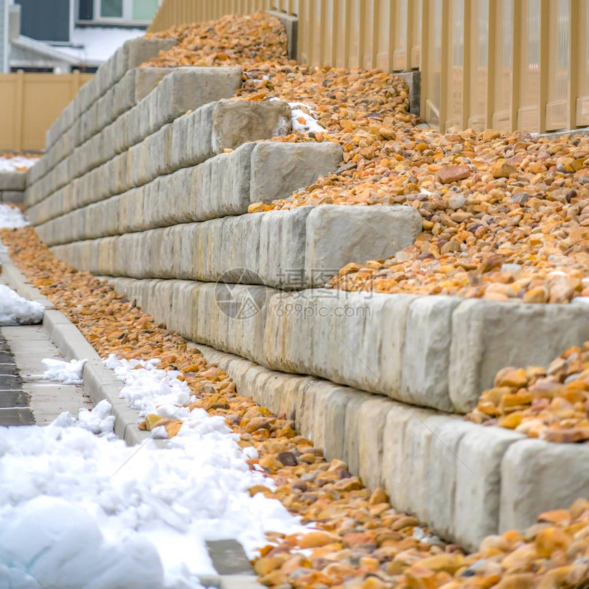 方形框架分层混凝土砌块和木栅栏在冬天有雪的道路旁在背景中可以看到房图片