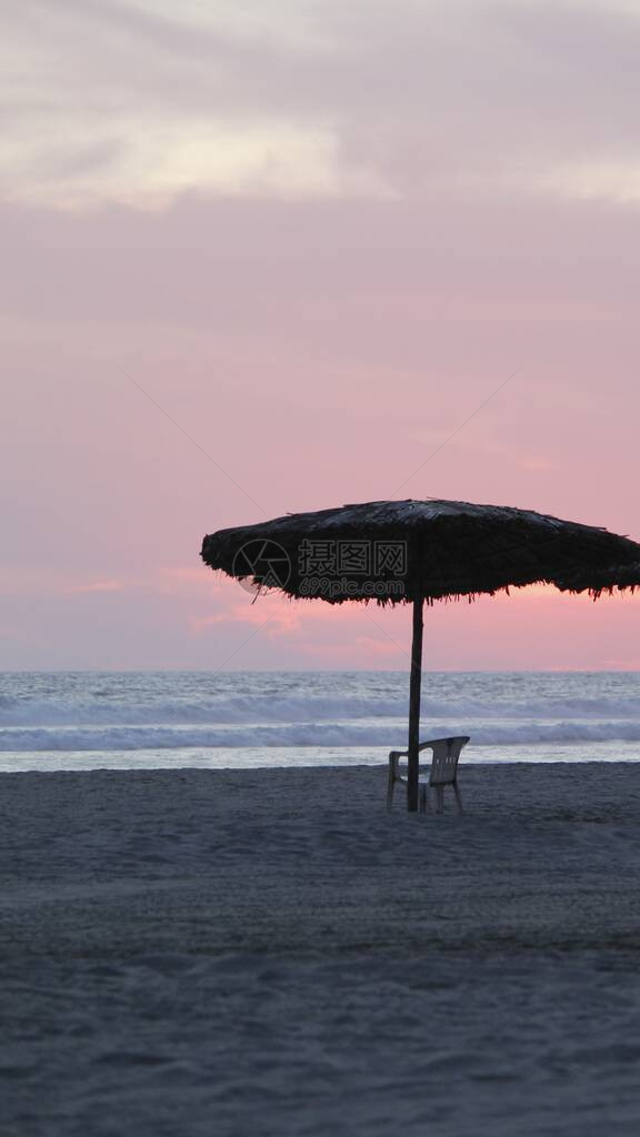 日落时在海滩上用干棕榈叶和空椅图片