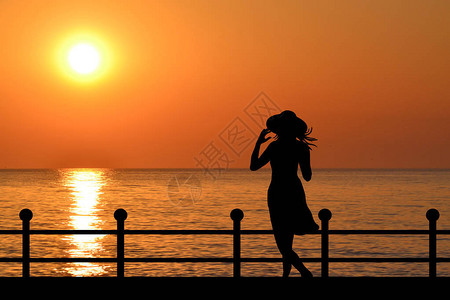 日出时在海滨戴帽子的女人的剪影图片