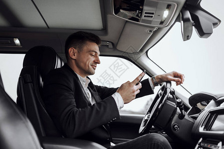 喜悦的商人在坐汽车时看智能手机屏幕的侧面景象图片