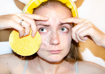 一位欧洲女孩正在将韩国化妆品涂在她的面膜上清洁毛孔油脂粉刺皱纹一个有皮肤问题的女孩的特写脸摩丝喷雾面部磨砂和洗面奶图片
