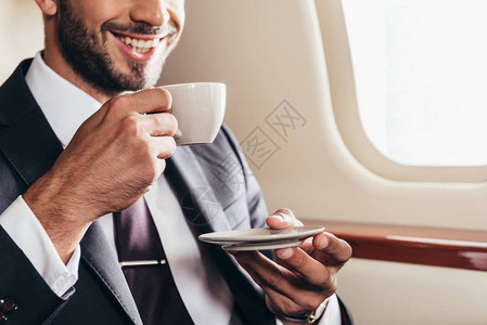 在私人飞机上端咖啡杯的西装服中笑图片