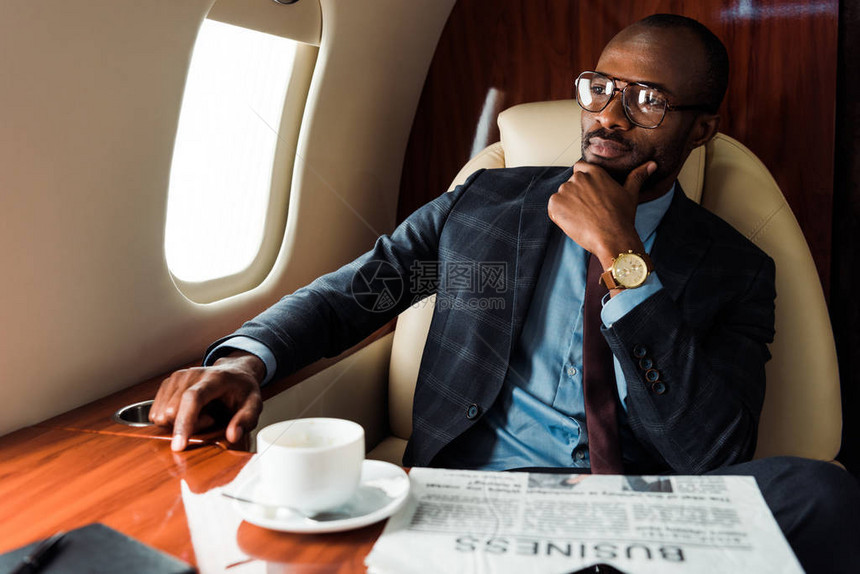 在商业报纸和私人飞机杯旁戴眼镜的非洲美国商人有选择地聚焦于商业报纸图片