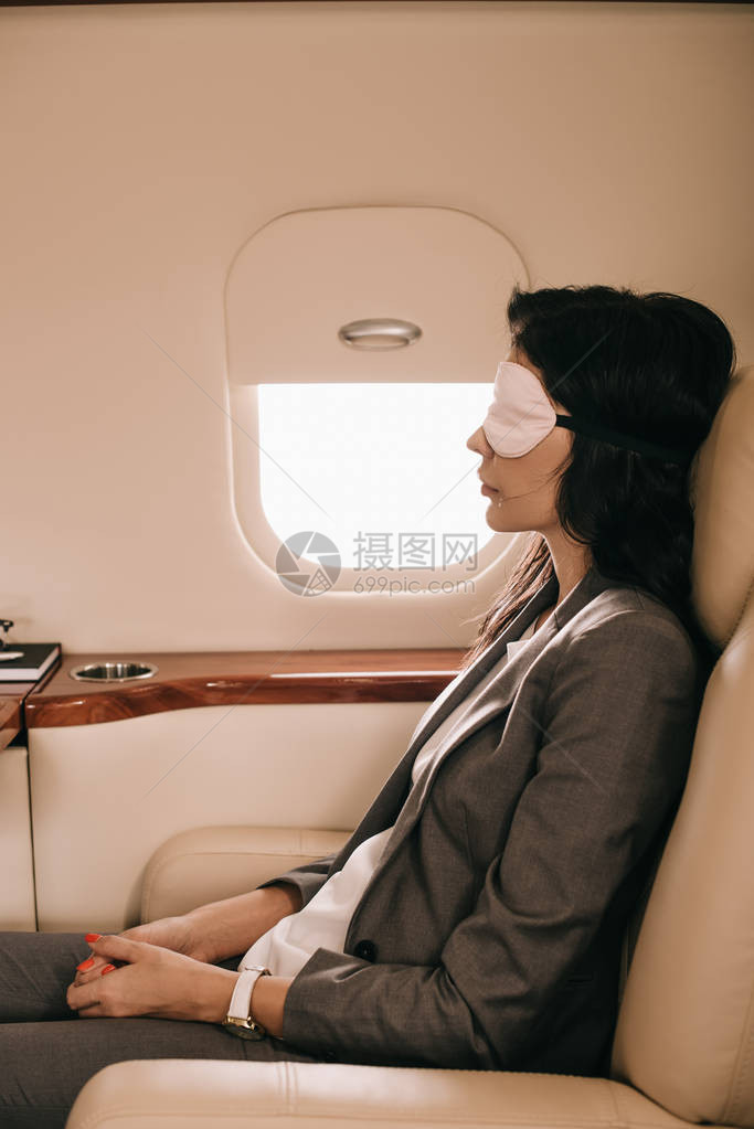 坐在私人飞机上靠近飞机窗的睡面罩图片