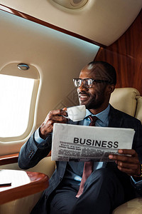 戴着眼镜持有商业报纸和私人飞机杯子的非洲商人图片