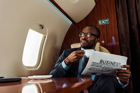 在私人飞机上拿着商业报纸和杯子的玻璃杯中图片