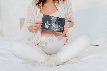 孕妇用超声波扫描婴儿时与双腿坐在床上的割切式眼部图片