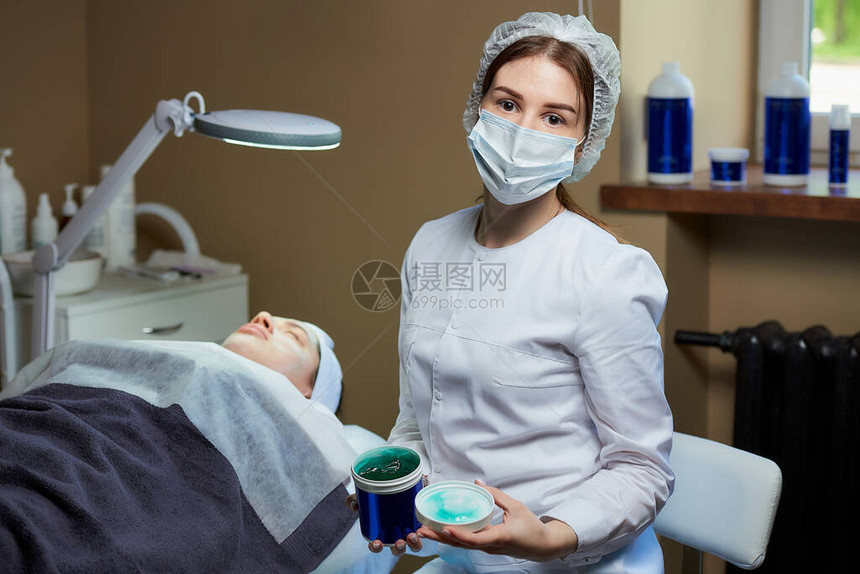 一位戴着手术面罩的女美容师在美容办公室的全电动美容床上与患者身边的护肤凝胶合影在美容院进行皮图片