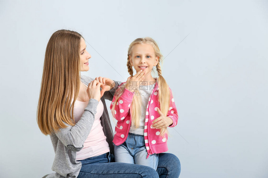 小聋哑女孩和母亲在轻背景使用手语的幼聋图片