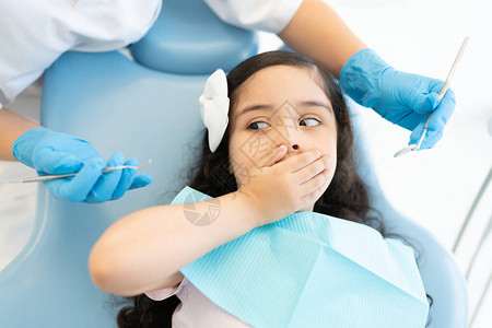恐惧的西班牙裔女孩在治疗期间用牙医手持工具时图片