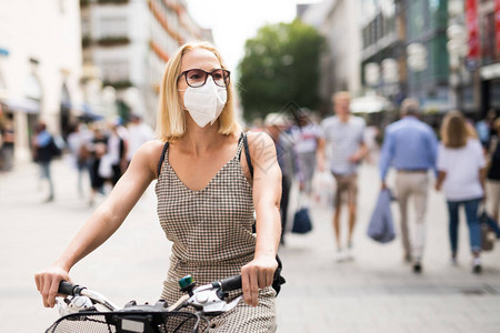 在城市街道上骑自行车的妇女在公共场合戴着医用口罩图片