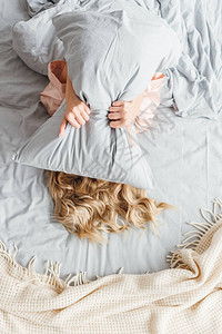 女青年用枕头蒙面躺在床上图片