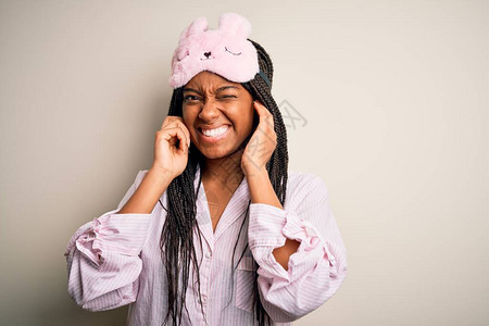 身穿粉红色睡衣和睡面罩的年轻非洲女在孤立的背景下用手指遮住耳朵图片