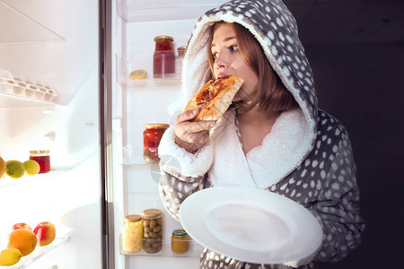 青少年女孩晚上在冰箱附近吃不健康图片