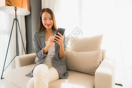 在客厅区使用会说话的手机和坐在沙发椅上的美丽亚洲图片