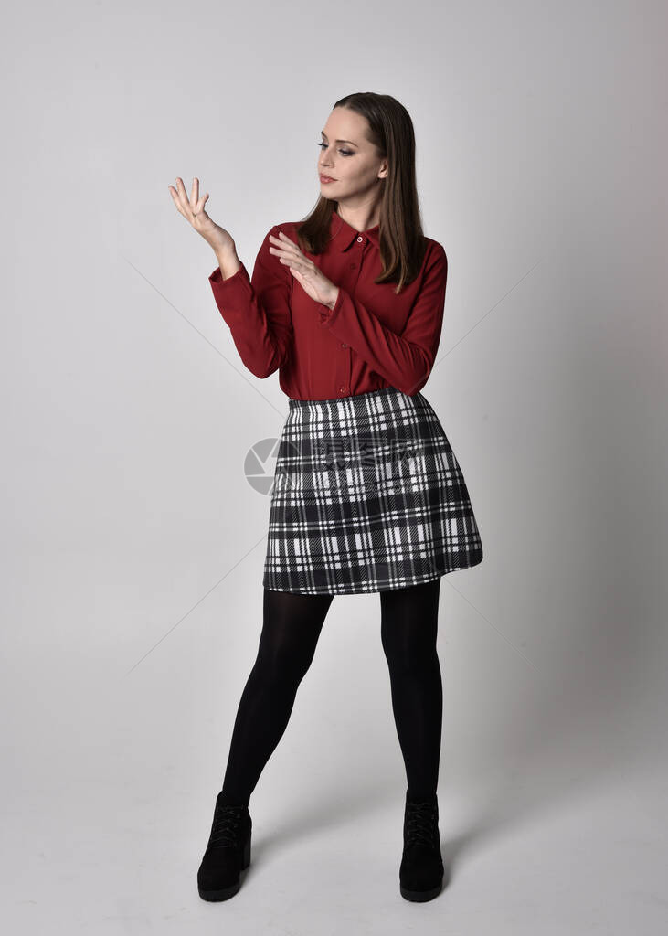 一个漂亮的黑发女孩穿着红色衬衫和格子裙搭配紧身裤和靴子的全长肖像站立姿势与手势反图片