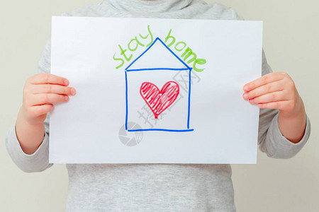 孩子的手拿着红心房子的照片写着待在家里科罗图片