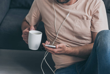 男人在耳机里听音乐和拿着咖啡杯时使用智图片