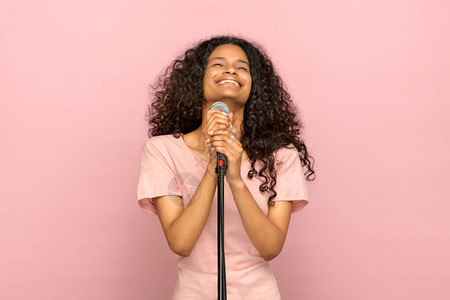 微笑着快乐的年轻黑人女孩歌唱在麦克风中图片