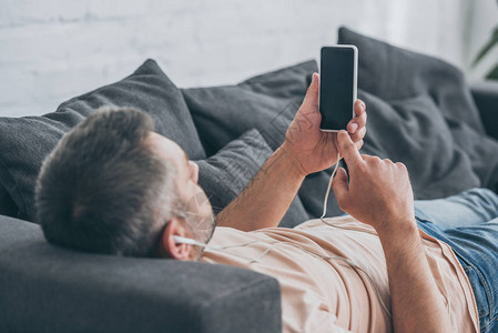 成人男子在睡沙发时用耳机听音乐图片