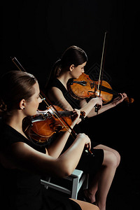两名专业音乐家在黑暗舞台的小提琴上背景图片