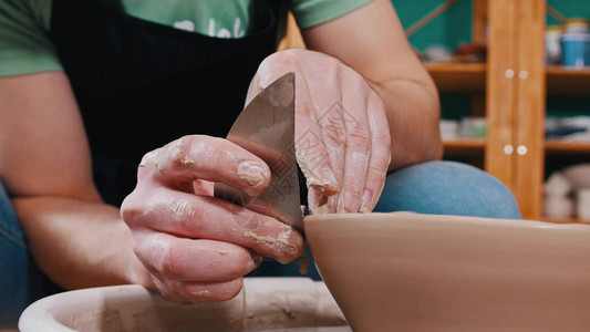 波特Pottery主人正在帮助用一个特殊的金属块来平滑粘土碗的图片