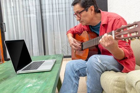 坐在沙发上坐在家里的男子在家中接受在线吉他课图片
