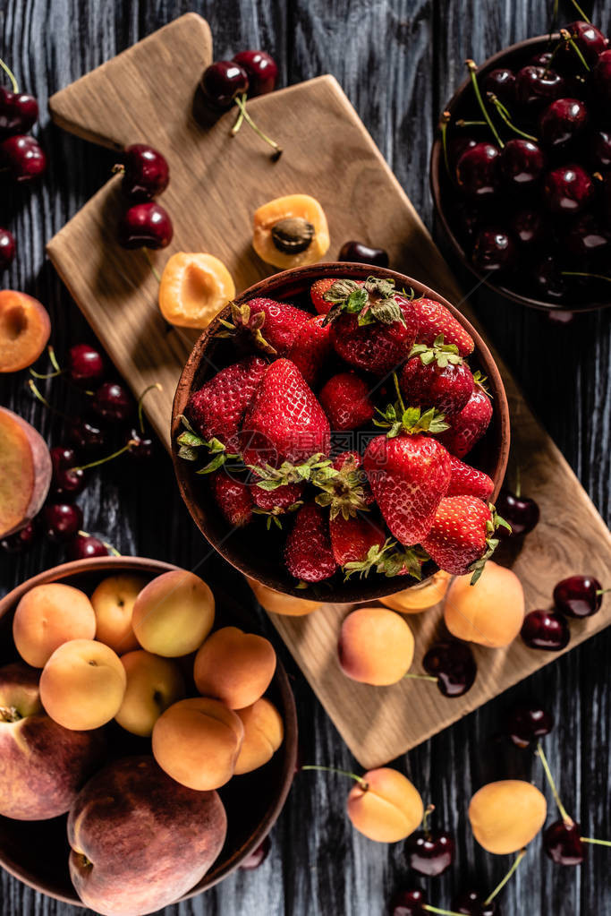 木桌上放着樱桃草莓桃子和杏子的碗顶视图图片