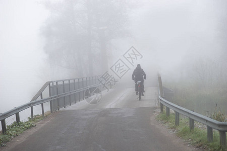 在阴暗的秋天在大雾中桥上骑自行车的骑图片
