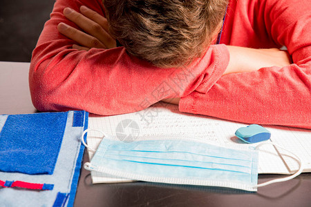 沮丧的男孩躺在书写材料上在家中教学时图片