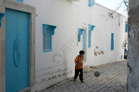 一个男孩在北非突尼斯北部突尼斯市附近的西迪布赛义德老城踢足球图片