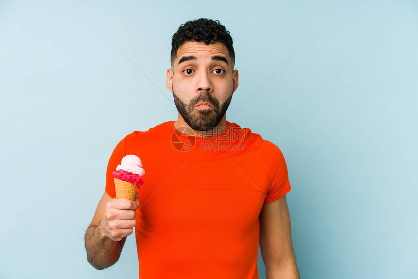 年轻拉丁男子拿着冰淇淋孤立的肩膀和睁图片