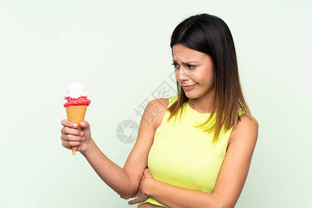 在孤立的绿色背景和悲伤的表情上拿着玉米角冰淇淋图片