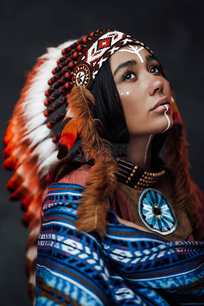 一个有魅力的年轻美国印第安女穿着传统羽毛帽和深底衣服近身肖像图片