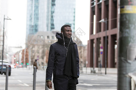 英俊的黑人男子听着耳机走在城市街道上图片