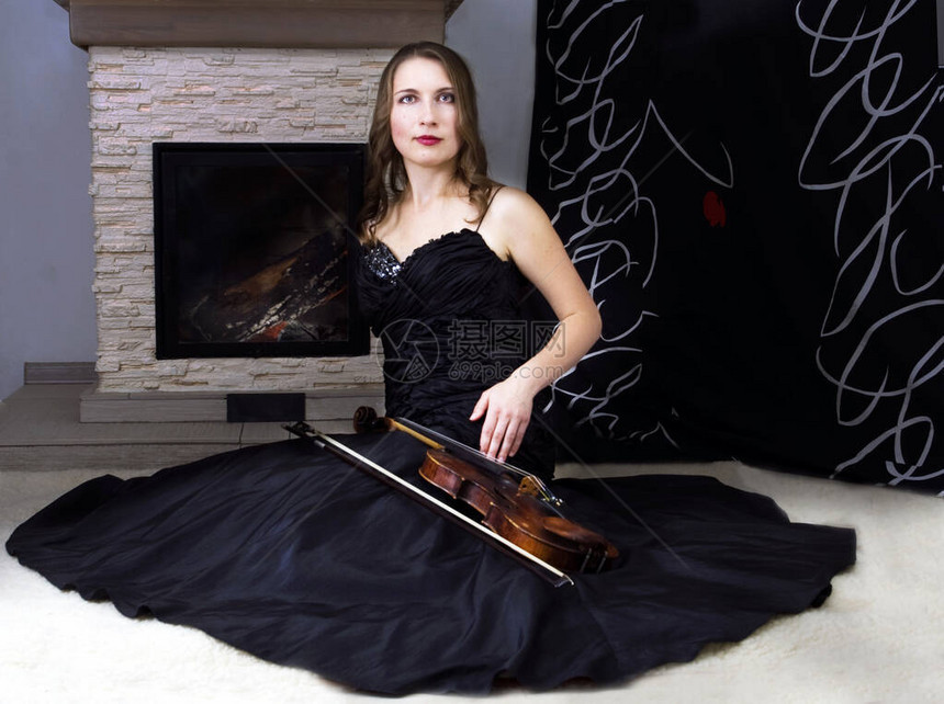 身着黑裙子的小提琴手坐在壁炉附近图片