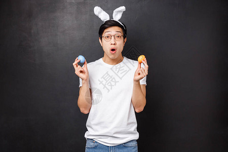 惊讶的年轻亚洲小伙在兔耳朵拿着彩蛋作为学习女朋友的传统图片