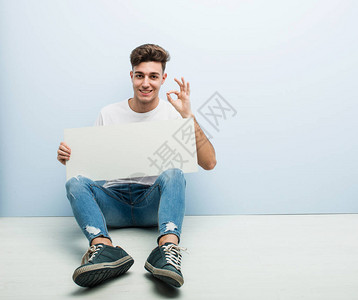 年轻男子拿着标牌坐在他家的地板上图片