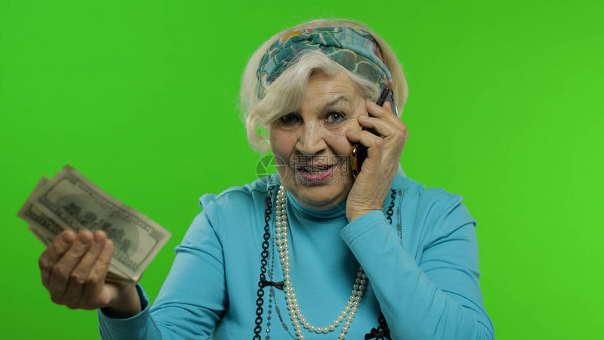 老年时尚老奶白种人成熟女人在手机上情绪化地交谈并展示钞票色度键背景有智能手机的老祖母在时尚衣图片