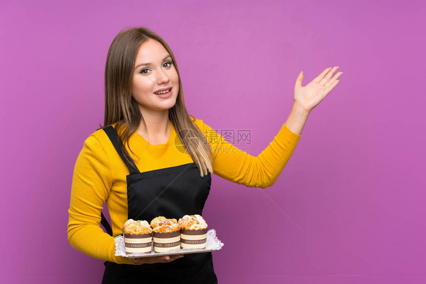 年轻女孩拿着许多不同的小蛋糕在孤立的紫色背景上手伸到侧面图片