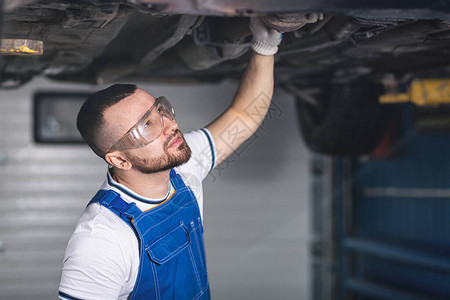 一位穿着工作服的年轻汽车修理工在他的工作场所修理汽车的悬架图片