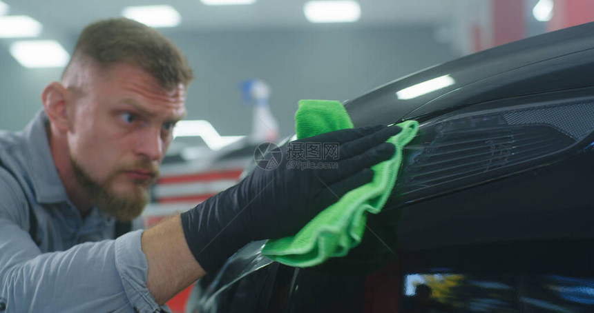在车库中清洗车辆时用手套戴胡子的男子喷洒水和擦图片