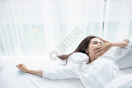 亚洲女人美丽的年轻微笑女人坐在白床上睡觉图片