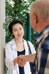 漂亮微笑的年轻越南医生在家探望老人并讨论治疗过程图片