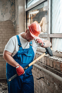 身穿特别制服的疲劳工人在建筑工地用防护头盔和手握大锤图片