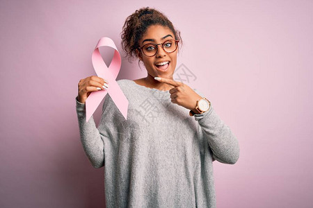 年轻的非洲裔美国黑人女孩在孤立的背景上拿着粉色癌症丝带图片