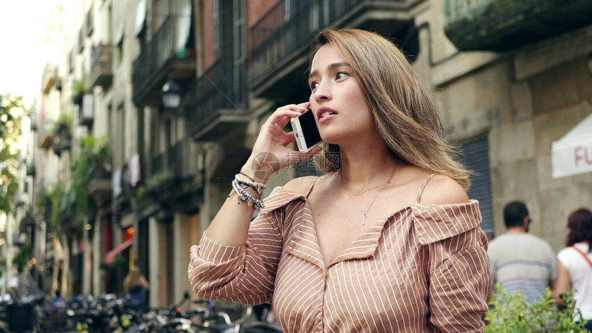 微笑的女人在慢动作中在城市街道上用手机说话的画像关闭了漂亮的女孩打电话给城市背景专注的女人在户图片